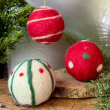 Three handmade felted Christmas ornaments on a wooden surface with greenery.