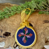 Decorative ornament with embroidered design on a wooden surface with greenery